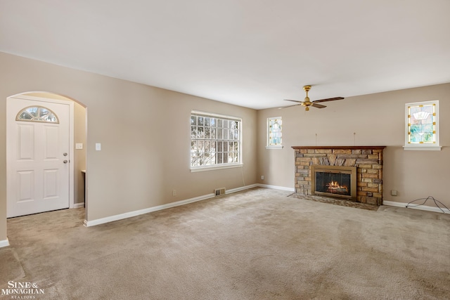 unfurnished living room featuring plenty of natural light, light carpet, a stone fireplace, and ceiling fan