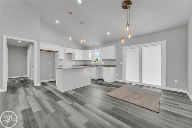 kitchen with stone counters, pendant lighting, high vaulted ceiling, white cabinetry, and a center island