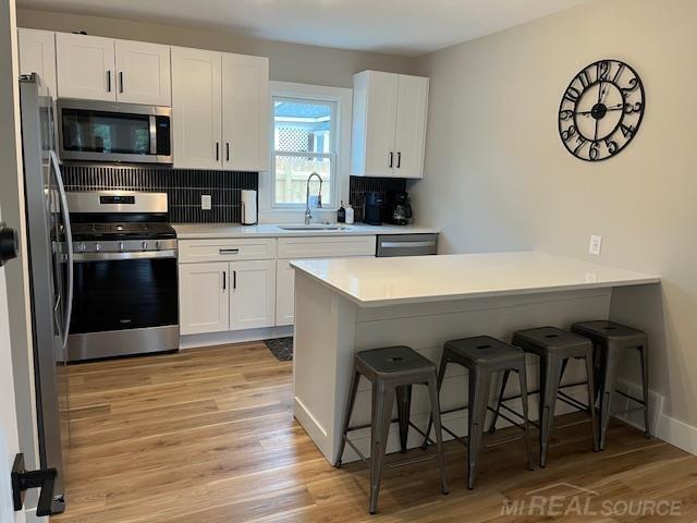 kitchen with a kitchen bar, sink, white cabinetry, appliances with stainless steel finishes, and kitchen peninsula