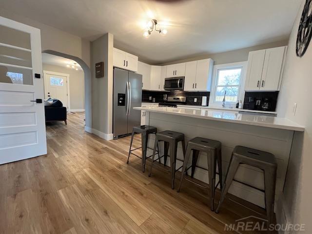 kitchen with a breakfast bar area, white cabinetry, tasteful backsplash, light wood-type flooring, and appliances with stainless steel finishes