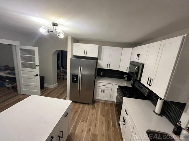 kitchen featuring stainless steel appliances, an inviting chandelier, white cabinets, and light hardwood / wood-style floors