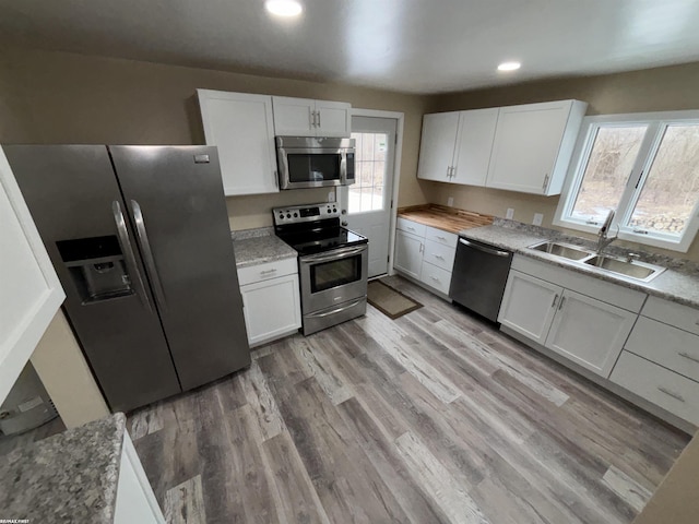 kitchen with stainless steel appliances, white cabinetry, sink, and light hardwood / wood-style flooring