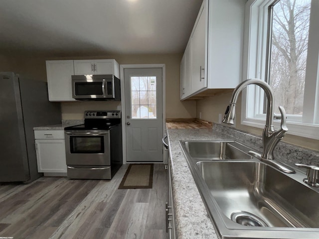 kitchen with light wood-type flooring, appliances with stainless steel finishes, sink, and white cabinets