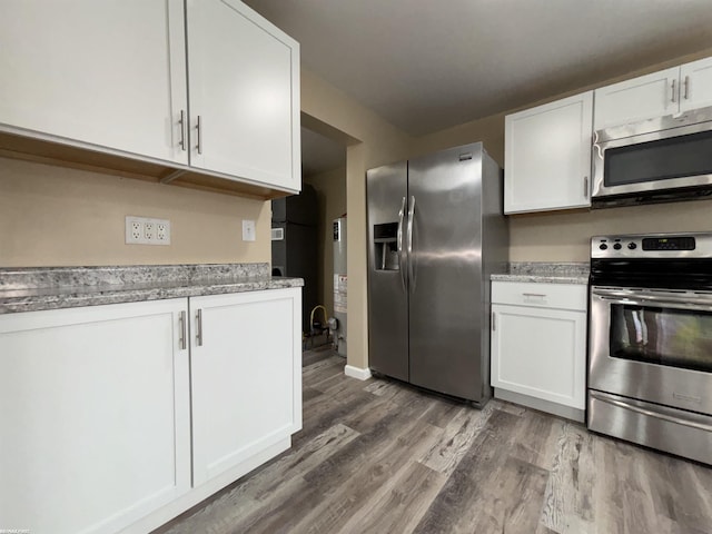 kitchen featuring stainless steel appliances, white cabinetry, light stone countertops, and wood-type flooring