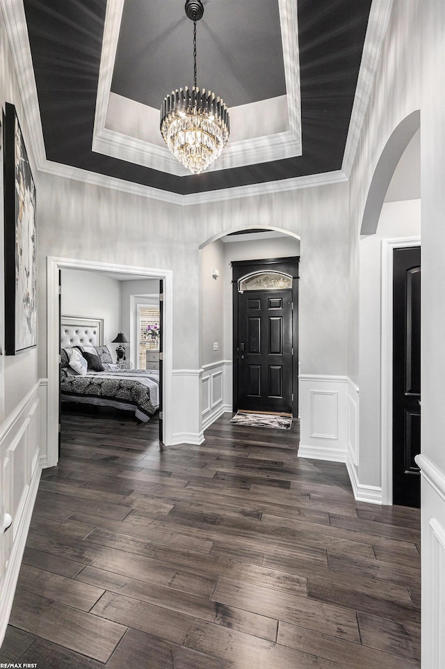 entryway featuring dark wood-type flooring, ornamental molding, a raised ceiling, and a chandelier