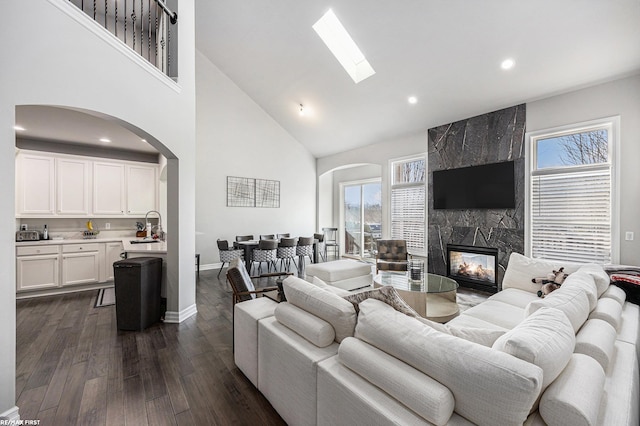 living room with sink, dark wood-type flooring, a skylight, high vaulted ceiling, and a fireplace