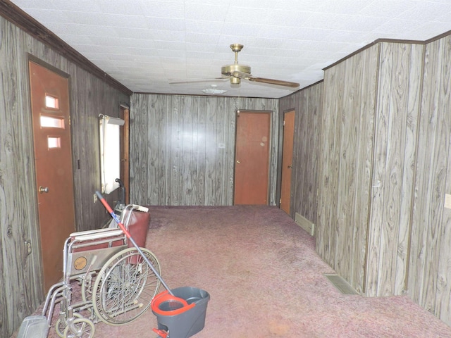 interior space with crown molding, carpet, wooden walls, and ceiling fan