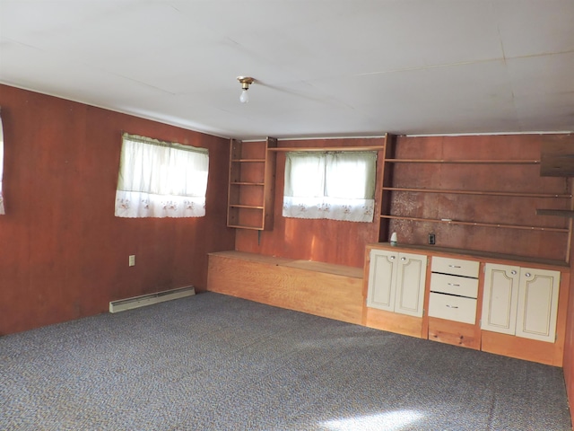 unfurnished living room with a baseboard radiator, plenty of natural light, carpet flooring, and wood walls