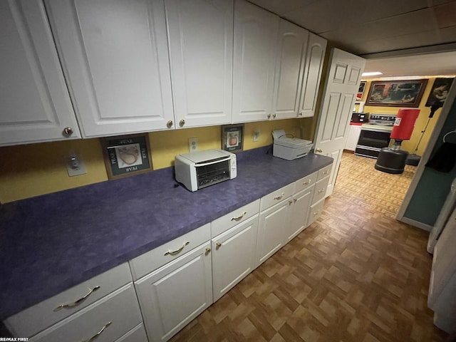 kitchen featuring stove, parquet floors, and white cabinetry