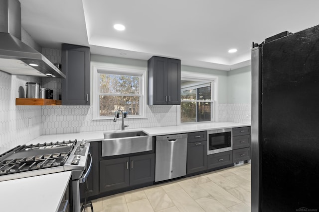 kitchen with wall chimney exhaust hood, sink, appliances with stainless steel finishes, a tray ceiling, and backsplash