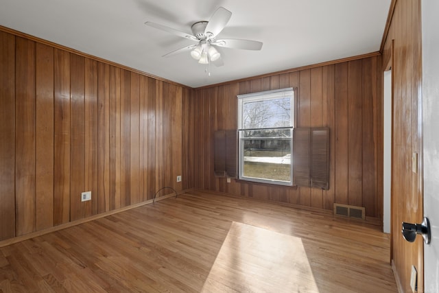 empty room with ceiling fan, wooden walls, and light wood-type flooring