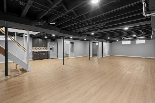 basement featuring stainless steel refrigerator with ice dispenser and light wood-type flooring