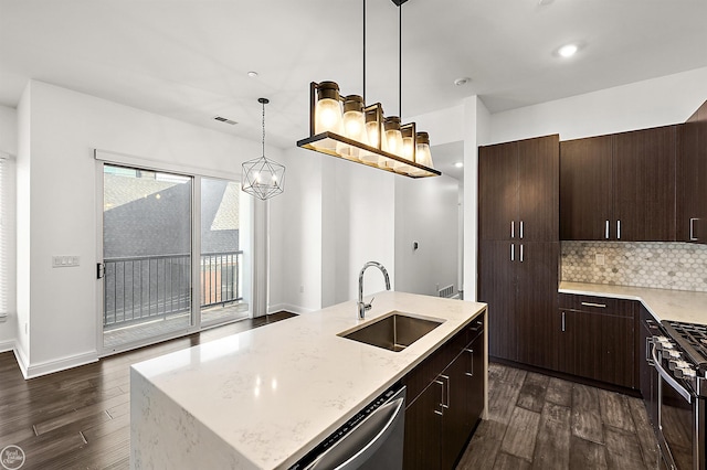 kitchen featuring dark wood-type flooring, sink, decorative light fixtures, appliances with stainless steel finishes, and an island with sink