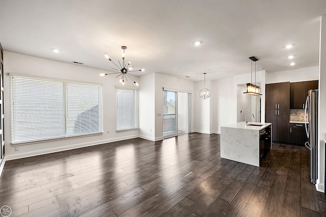 kitchen with sink, stainless steel fridge, dark brown cabinetry, an island with sink, and a chandelier