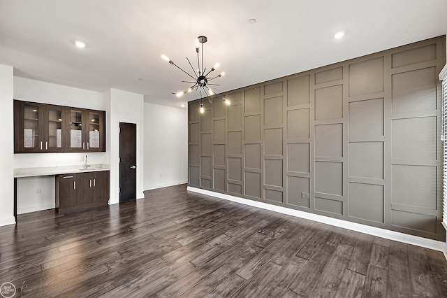 unfurnished living room with sink, an inviting chandelier, and dark hardwood / wood-style floors