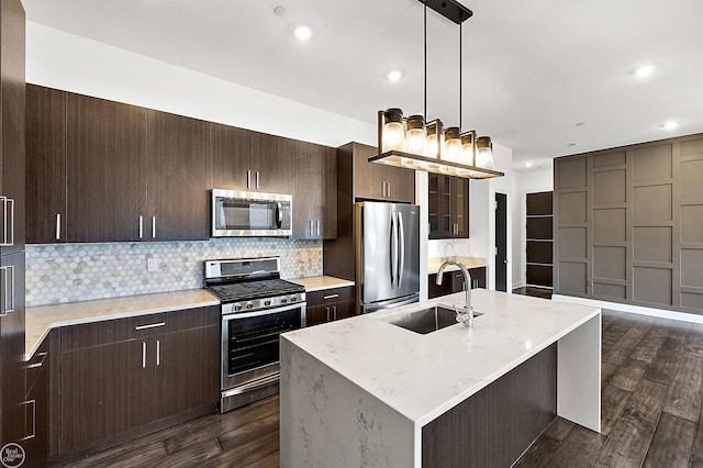 kitchen featuring appliances with stainless steel finishes, sink, dark hardwood / wood-style flooring, hanging light fixtures, and a kitchen island with sink