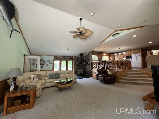 living room with ceiling fan, light colored carpet, vaulted ceiling, and a wood stove