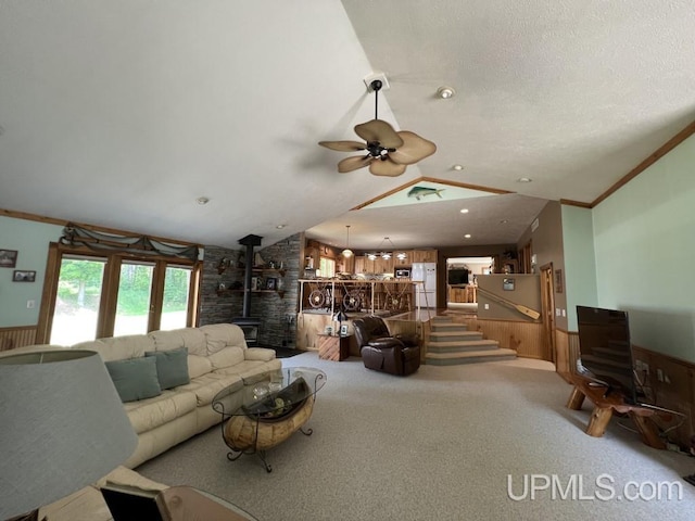 carpeted living room with vaulted ceiling, ornamental molding, ceiling fan, and a wood stove