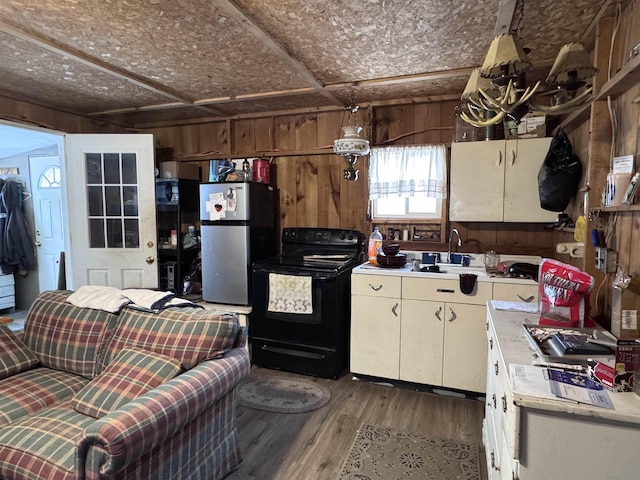 kitchen with wood walls, sink, stainless steel fridge, hardwood / wood-style flooring, and black electric range