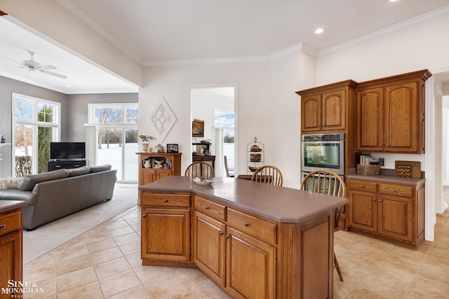 kitchen with light tile patterned floors, ceiling fan, ornamental molding, a kitchen island, and stainless steel double oven