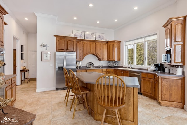 kitchen with sink, appliances with stainless steel finishes, a kitchen breakfast bar, ornamental molding, and a kitchen island