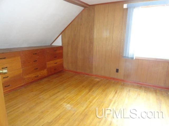 bonus room with vaulted ceiling with beams, light hardwood / wood-style flooring, and wood walls