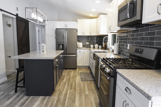 kitchen with appliances with stainless steel finishes, a breakfast bar, white cabinetry, hanging light fixtures, and a barn door