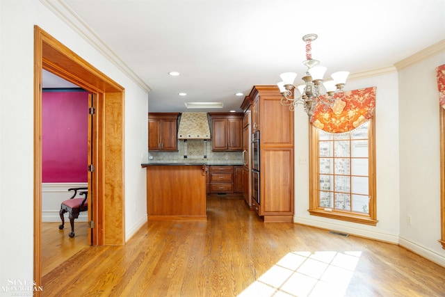 kitchen featuring hanging light fixtures, crown molding, light wood-type flooring, and wall chimney exhaust hood