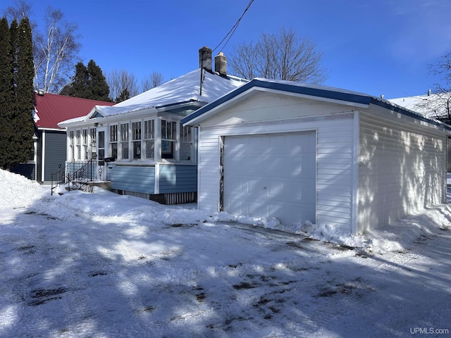 view of snowy exterior featuring a garage and a sunroom