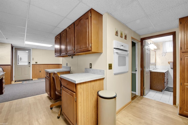 kitchen featuring a paneled ceiling, oven, light hardwood / wood-style flooring, and wood walls