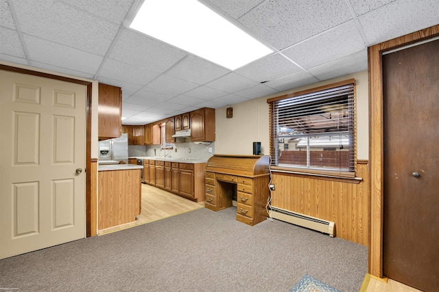 kitchen with baseboard heating, a drop ceiling, light carpet, stainless steel fridge with ice dispenser, and wood walls