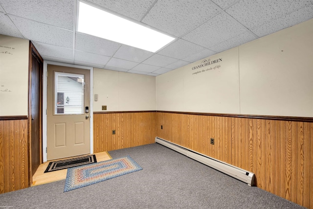 interior space featuring a baseboard radiator, a drop ceiling, and wood walls