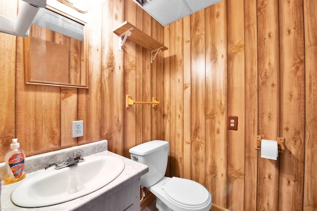 bathroom featuring vanity, wooden walls, and toilet