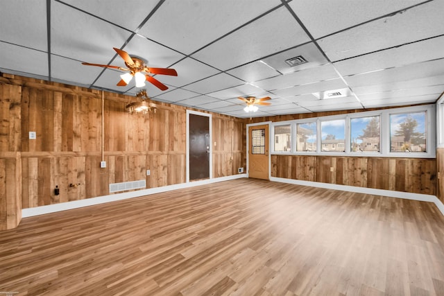 unfurnished living room with ceiling fan, wooden walls, hardwood / wood-style floors, and a drop ceiling