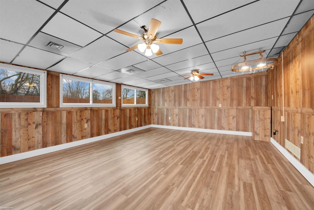 basement with a paneled ceiling, wooden walls, and light hardwood / wood-style floors