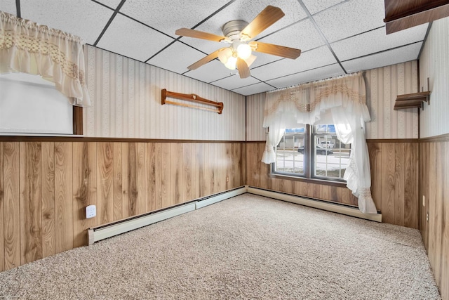 unfurnished room featuring ceiling fan, wooden walls, carpet flooring, and a drop ceiling