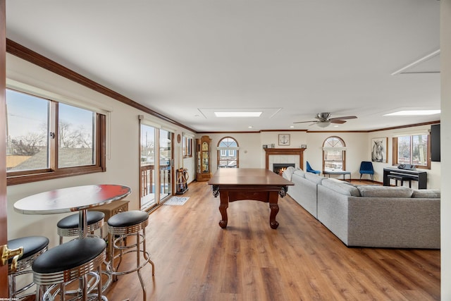 rec room featuring crown molding, light wood-type flooring, ceiling fan, and a fireplace