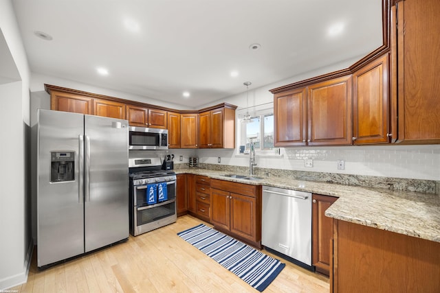 kitchen with decorative light fixtures, sink, light stone counters, light hardwood / wood-style floors, and stainless steel appliances