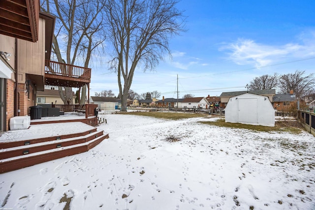 yard covered in snow with a wooden deck and a shed