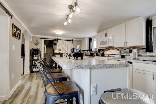 kitchen featuring white appliances, a breakfast bar, white cabinetry, backsplash, and a barn door