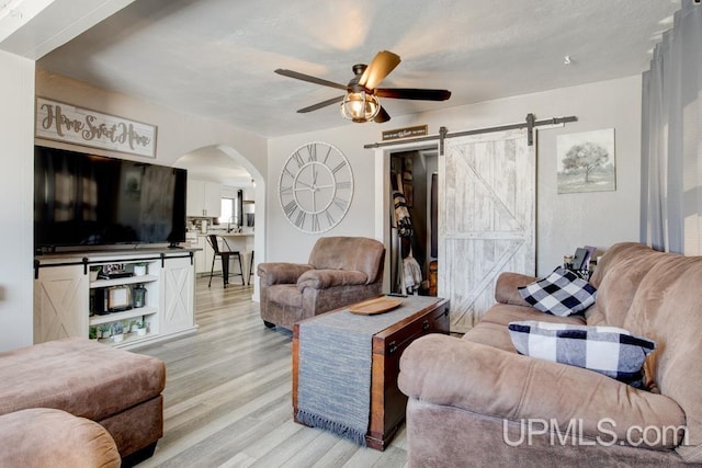 living room featuring a barn door, ceiling fan, and light wood-type flooring