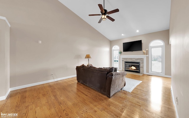 living room with a tile fireplace, high vaulted ceiling, ceiling fan, and light hardwood / wood-style floors