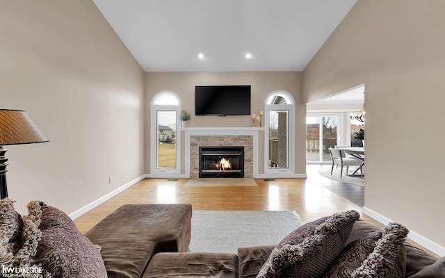 living room with a tiled fireplace, high vaulted ceiling, and light wood-type flooring