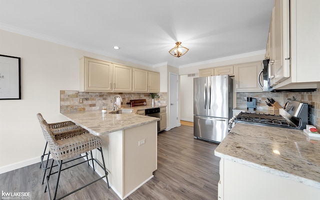 kitchen with sink, a kitchen bar, stainless steel appliances, light stone countertops, and cream cabinetry