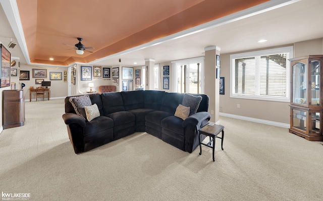 carpeted living room with ceiling fan, a raised ceiling, and decorative columns