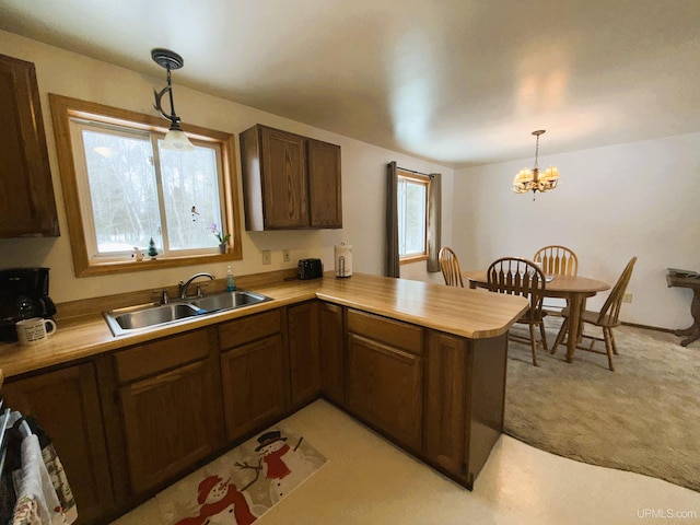 kitchen with pendant lighting, sink, a notable chandelier, light colored carpet, and kitchen peninsula