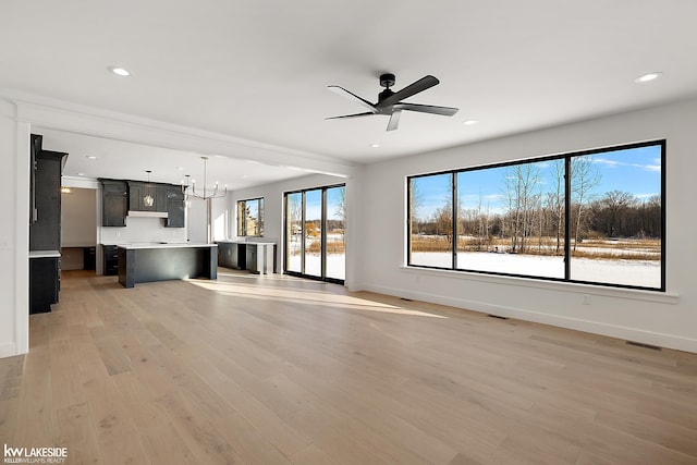 unfurnished living room with ceiling fan with notable chandelier and light wood-type flooring