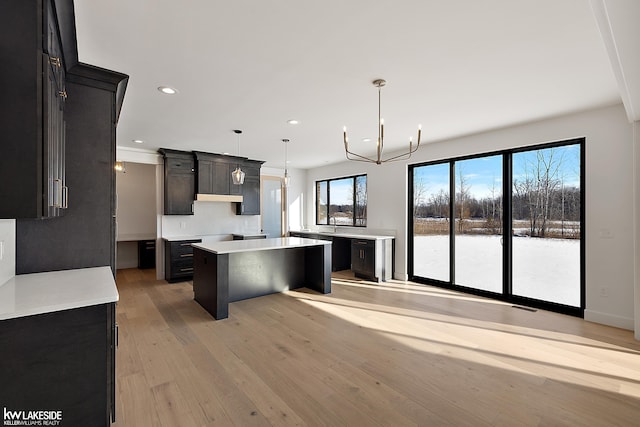 kitchen featuring pendant lighting, a center island, a notable chandelier, a water view, and light hardwood / wood-style flooring