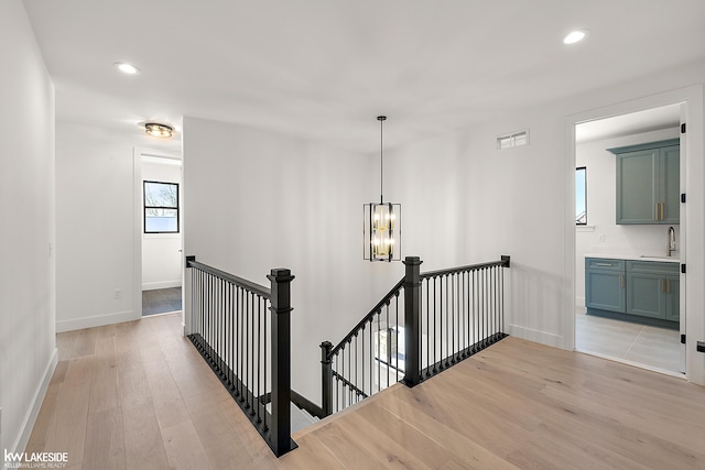 corridor with sink, an inviting chandelier, and light hardwood / wood-style flooring