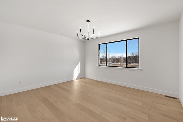 empty room with light wood-type flooring and a notable chandelier